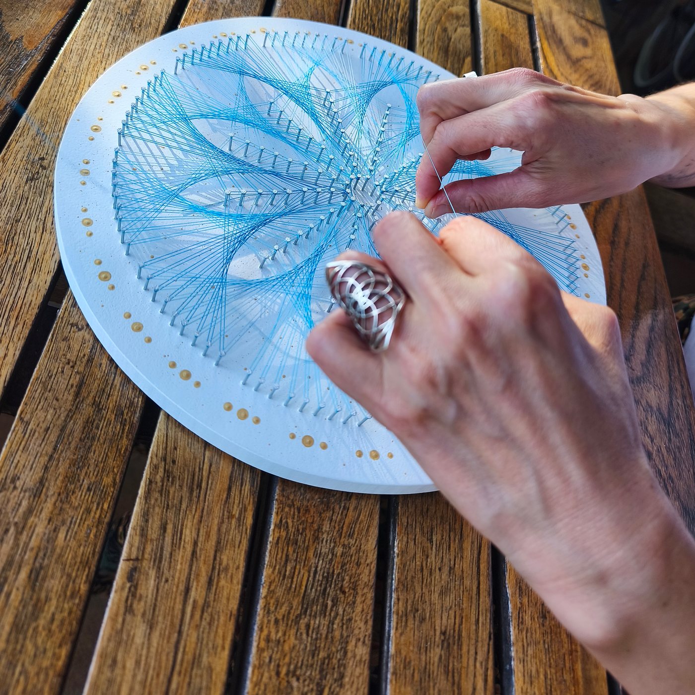 Les mans de Nohemí teixint el mandala de fil blau